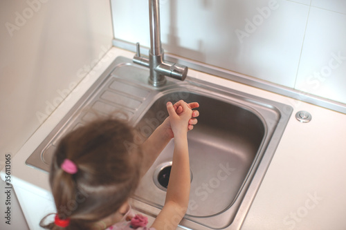 Little girl washing her hand. With soap under the tap. Kitchen interior.