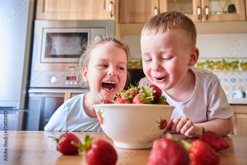 Two beautiful children in the kitchen eating strawberries and drinking milk.Children have fun. 
