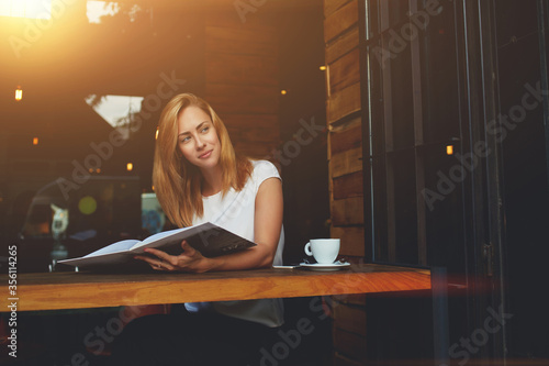 Young charming woman posing while sitting in cafe during coffee break,