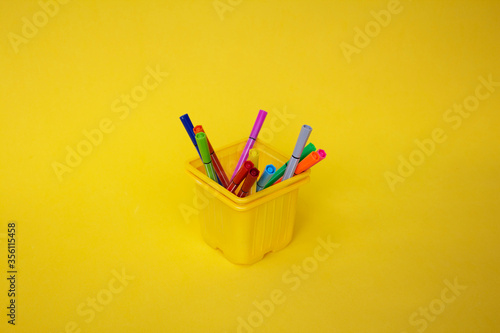 a set of new bright plastic colored markers, standing in a yellow glass on a yellow background. the concept of a stationery