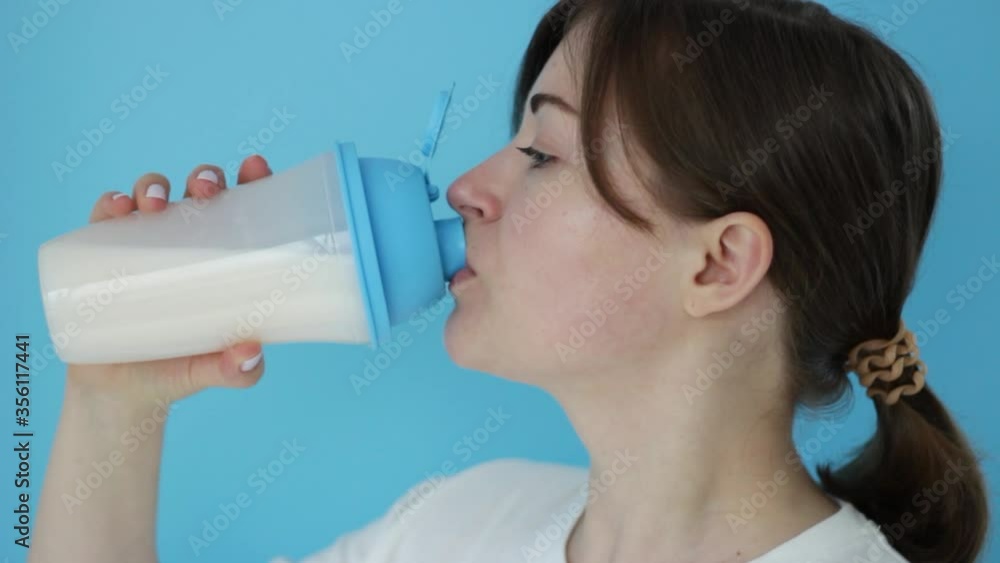 beautiful young girl drinks protein shaker on the blue background beautiful young girl drinks protein shaker on the blue background