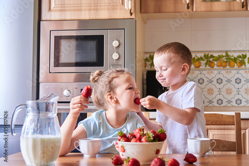 Two beautiful children in the kitchen eating strawberries and drinking milk.Children have fun. 