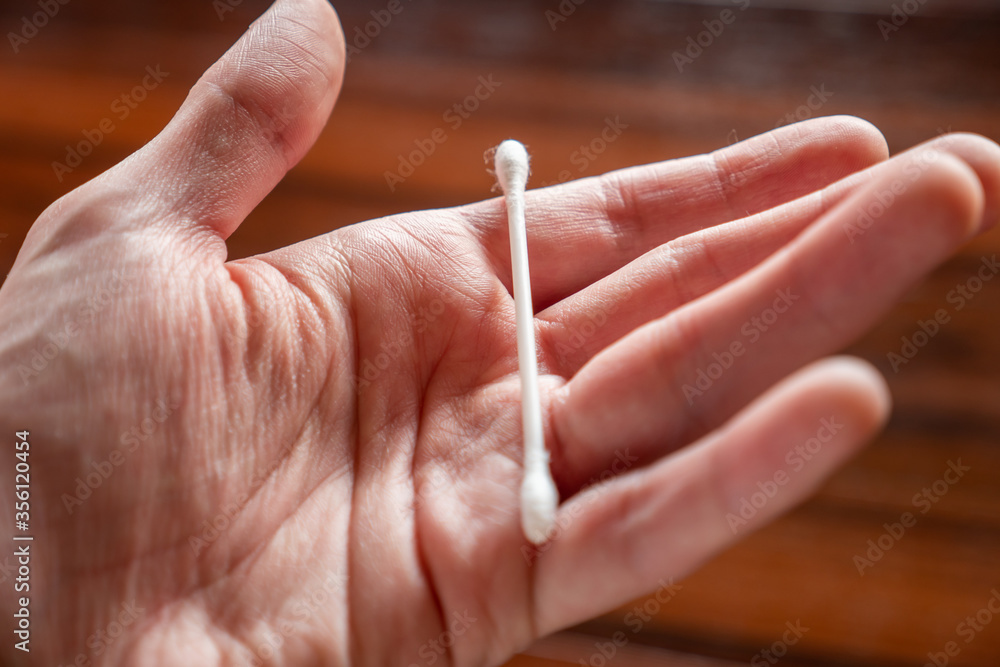 Una mano sujetando un bastoncillo de algodón para limpiarse los oídos. Una mano sujetando un bastoncillo de algodón para limpiarse los oídos.