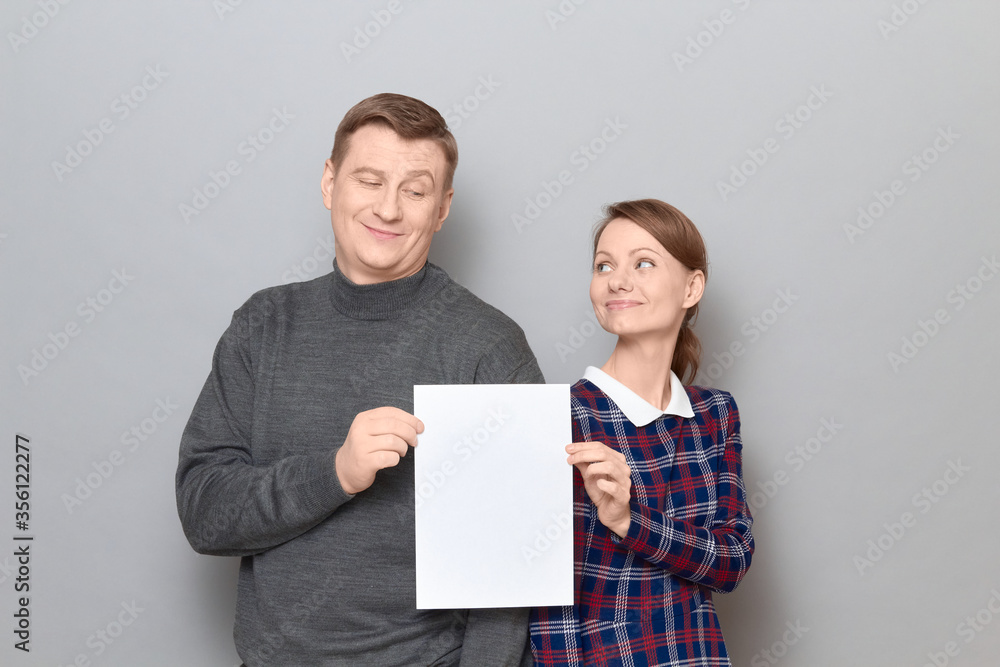 Portrait of adult couple holding together white blank paper sheet Portrait of adult couple holding together white blank paper sheet