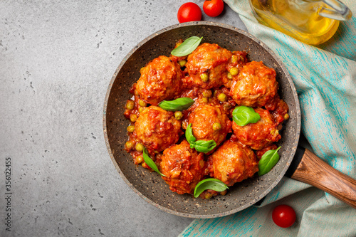Turkey meatballs  in tomato sauce  with green peas and basil leaves. Flat lay, grey concrete background.