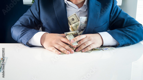 Fotografiet Greedy rich businessman filling his pockets with money.