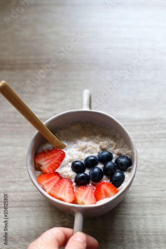Hand holding a bowl of rice and cinnamon porridge with blueberry and strawberry topping. Selective focus.