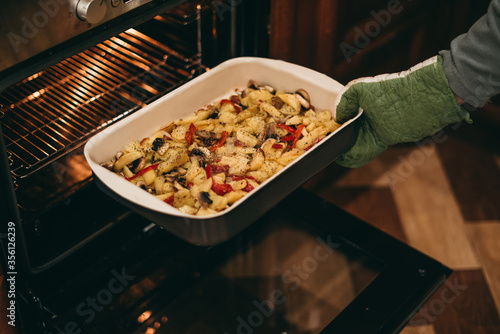 Home cooking in quarantine. Woman removes cooked, baked potatoes with mushrooms and spices from the oven.