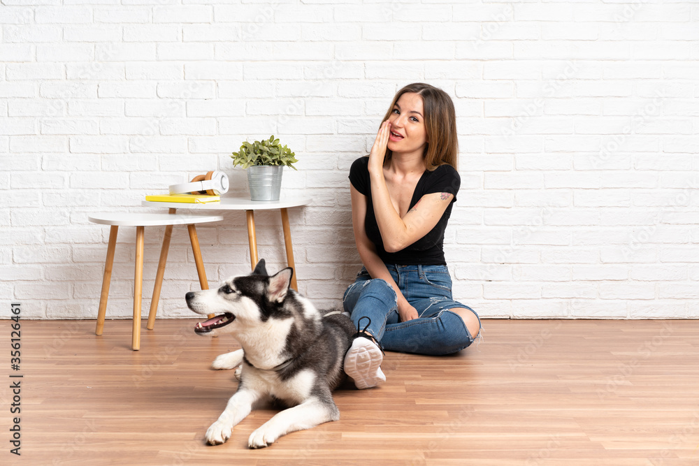 Young pretty woman with her husky dog sitting in the floor at indoors whispering something Young pretty woman with her husky dog sitting in the floor at indoors whispering something