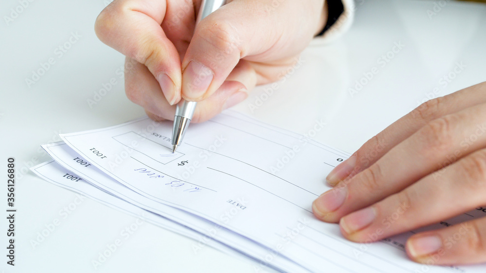 Businesswoman filling and signing banking cheque on office desk Businesswoman filling and signing banking cheque on office desk