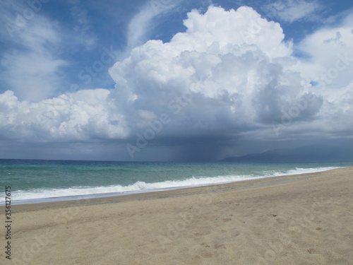 clouds over the sea. The seashore is a beach  the rain goes into the sea. Blue sky and rain cloud. The weather is rainy and sunny.Thundercloud over the sea. Beach before a thunderstorm. Rain and sun. 