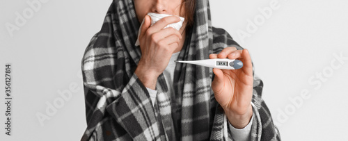 Fever and illness. Man coughs, covers his mouth with napkin and shows thermometer with high temperature