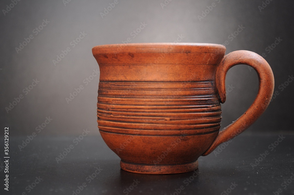 Clay cup against a dark background with the handle turned to the right Clay cup against a dark background with the handle turned to the right
