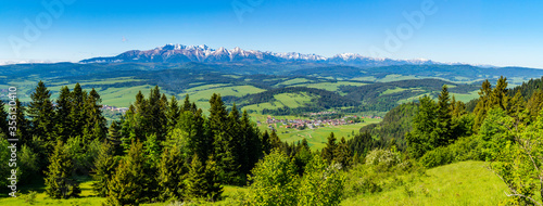 A wide panorama of the mountain range - Tatra Mountains. In the valley there is a village surrounded by forests, meadows and fields. Spring rural landscape.