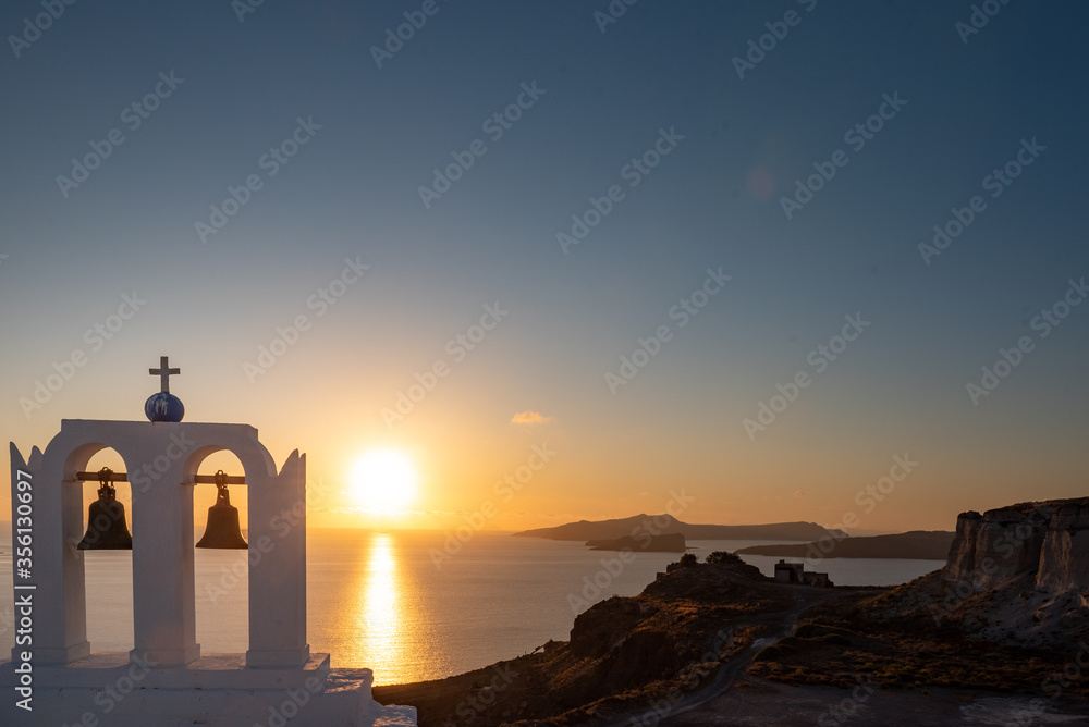 Sunset on Santorini  island, Greece.  Church with bell tower in foreground. Volcano in the background. 