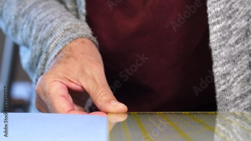 Elderly woman hand placing ruler on blue cotton fabric to guide a rotary cutter down a cutting mat. 