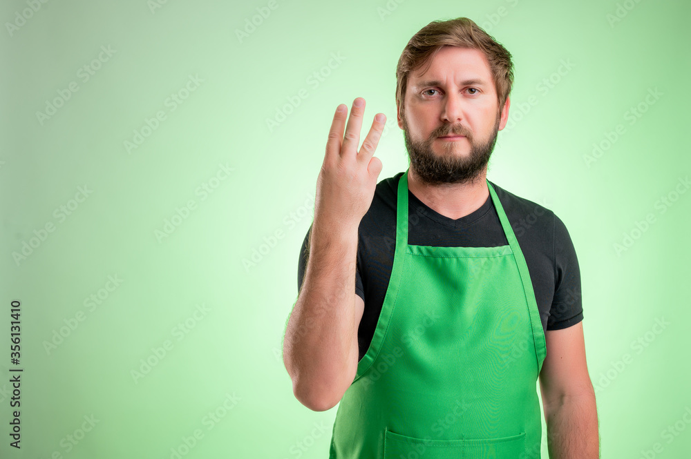 Fototapeta premium Supermarket employee with green apron and black t-shirt counting three with his fingers