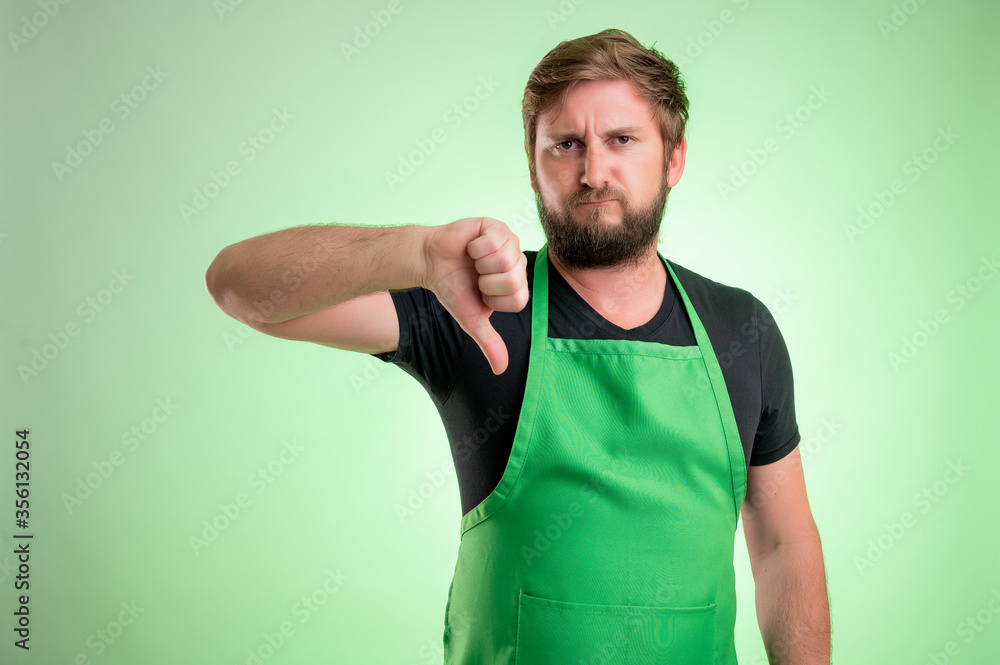 Supermarket employee with green apron and black t-shirt showing dislike Supermarket employee with green apron and black t-shirt showing dislike