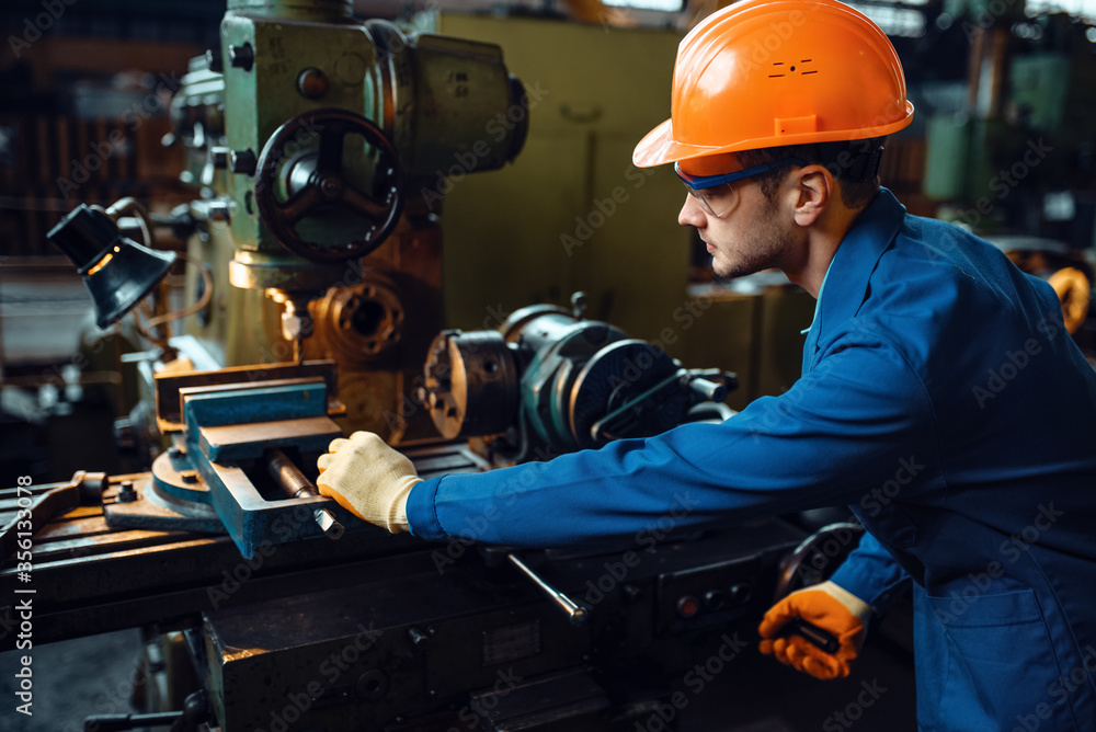 Worker in uniform and helmet works on lathe, plant Worker in uniform and helmet works on lathe, plant