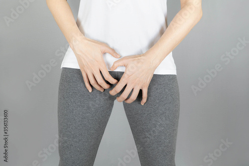 Cropped of woman in gray shorts put her hand on the genitalia area, Penis pain or Itching urinary Health-care concept on gray background with copy space