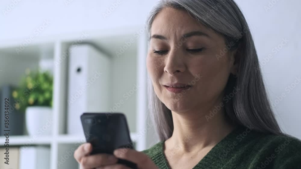 A calm good-looking mature businesswoman is using her smartphone working in the office A calm good-looking mature businesswoman is using her smartphone working in the office