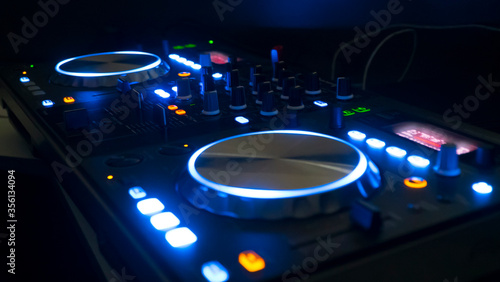 DJ sound control console for mixing dance music and laptop in disco club. Hands touching buttons sliders, playing electronic music on mixing deck, color illumination in nightclub dance party. Close up