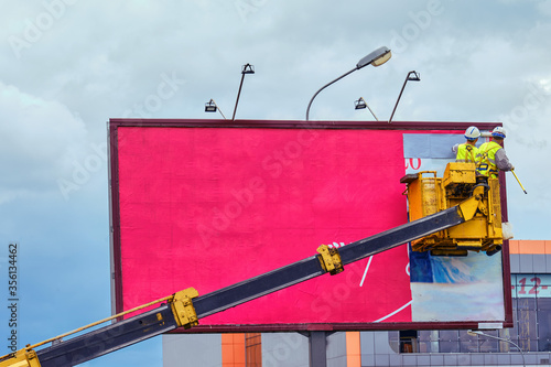 Obraz na plátně Two workers install red billboard on roadside of city street