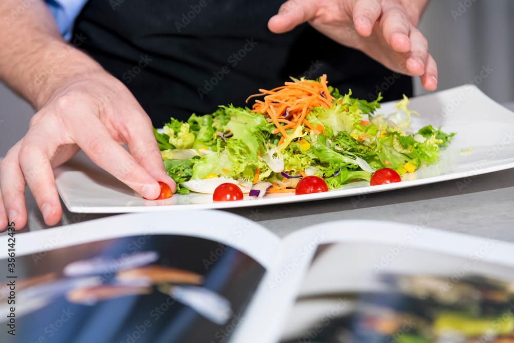 male hands adding the finishing touches to a delicious looking salad with an out of focus book at the front