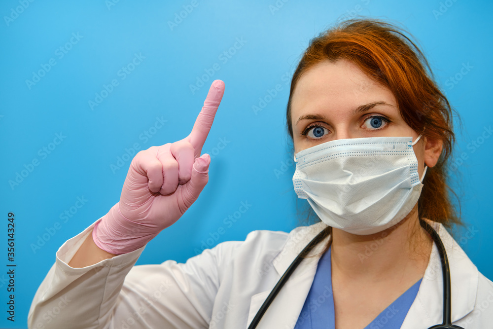 Doctor in a white uniform points up, a concept on a blue background. Face of the nurse's girl, close-up. Stay home. Doctor in a white uniform points up, a concept on a blue background. Face of the nurse's girl, close-up. Stay home.