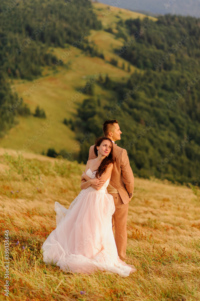 The bride and groom stand with their backs to each other against the backdrop of autumn mountains. Sunset. Wedding photography.