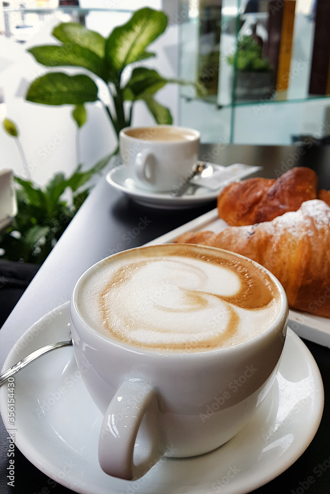 Cup of cappucino with croissant on black table in cafe Cup of cappucino with croissant on black table in cafe