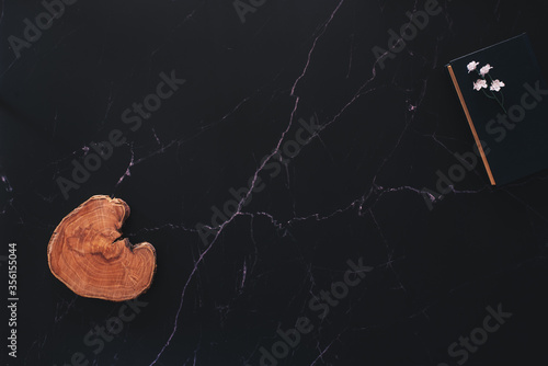 Flat lay of a floral arrangement and a wood piece and a book against black marble photo