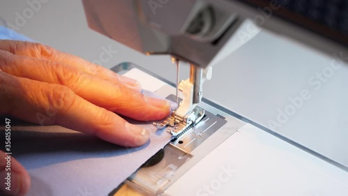 Female hands feeding sewing machine cotton fabric in slow motion. Needle stitching cloth material for a homemade face mask. 