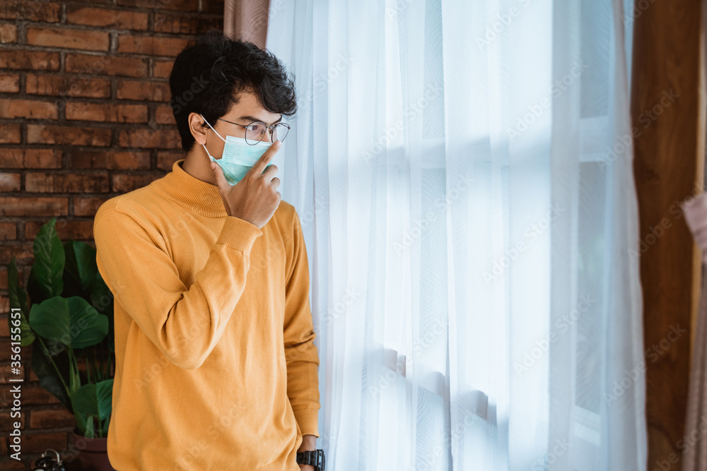 man wearing a mask looks sad when standing by the window man wearing a mask looks sad when standing by the window