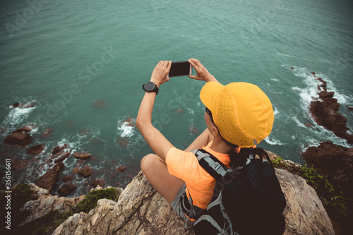 Woman hiker taking photo with smartphone on seaside cliff edge