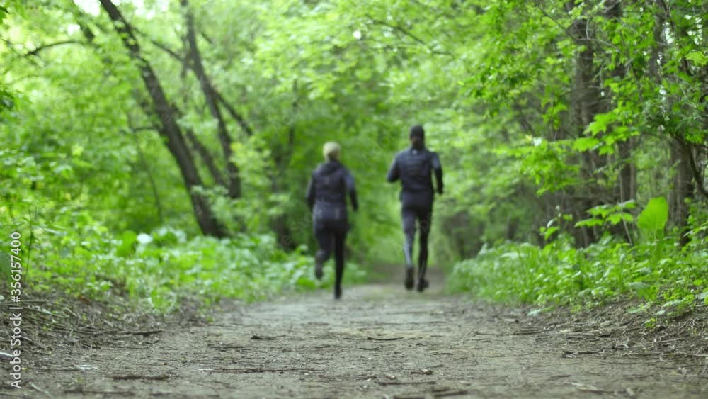 Running in a forest. Young woman and young man running on a forest trail on a summer day. Two friends go for a trail run in a forest. Low angle shot. Running in a forest. Young woman and young man running on a forest trail on a summer day. Two friends go for a trail run in a forest. Low angle shot.