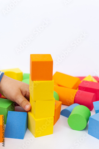 A child builds a pyramid of cubes on a white background. The boy's hand holds a cube.