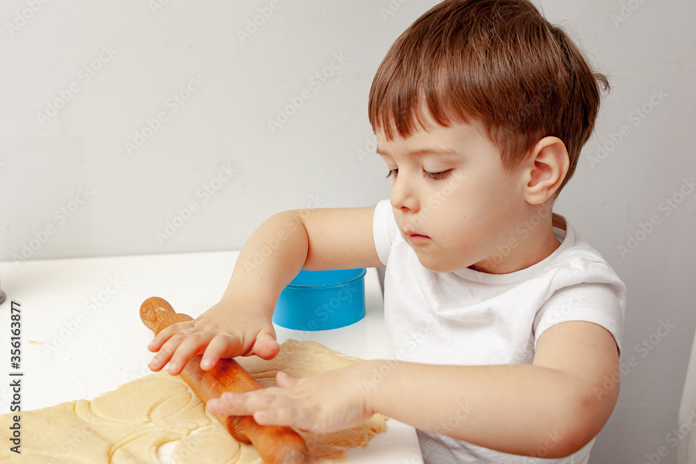 Little boy helps mother to cook making homemade coockies. Casual lifestyle in home interior, pretty child, holiday concept, rolling pin, coockie cutters and dough. Indoors, copy space. Little boy helps mother to cook making homemade coockies. Casual lifestyle in home interior, pretty child, holiday concept, rolling pin, coockie cutters and dough. Indoors, copy space.