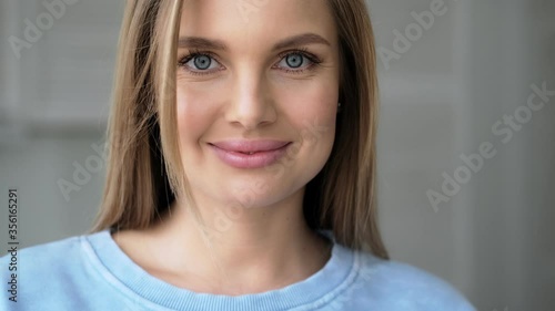 A happy glad young blonde woman is looking to the camera standing at home