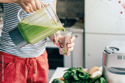 A woman pours a smoothie from a vitamin cocktail into a glass. Healthcare Cook at home.