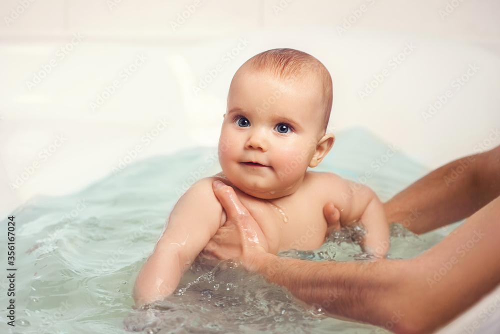 Hands of a careful unknown mother hold a small beautiful funny big-eyed baby. The concept of care and hygiene over children. Hands of a careful unknown mother hold a small beautiful funny big-eyed baby. The concept of care and hygiene over children.