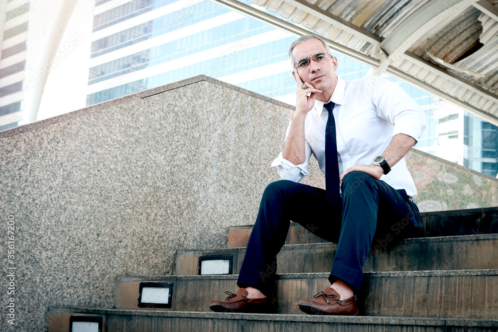 Senior businessman sitting on stairway outside office in downtown of modern city. Serious man resting chin on hand and thinking about his job. Senior businessman sitting on stairway outside office in downtown of modern city. Serious man resting chin on hand and thinking about his job.