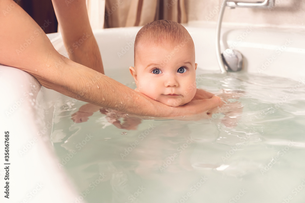 Hands of a careful unknown mother hold a small beautiful funny big-eyed baby. The concept of care and hygiene over children. Hands of a careful unknown mother hold a small beautiful funny big-eyed baby. The concept of care and hygiene over children.