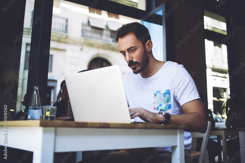 Young handsome man entrepreneur posing while sitting with open laptop computer
