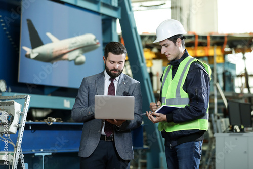 Portrait of a solid businessman with laptop and factory engineer controlling work process in a airplane manufactory. 
