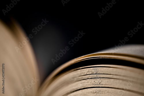 Open book with gold-like atmosphere on dark background, focus on pages at the right side. Narrow depth of field