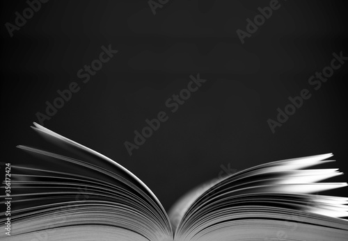 Open book (color) with narrow depth of field on black background. Black and White photo, space for text above the book