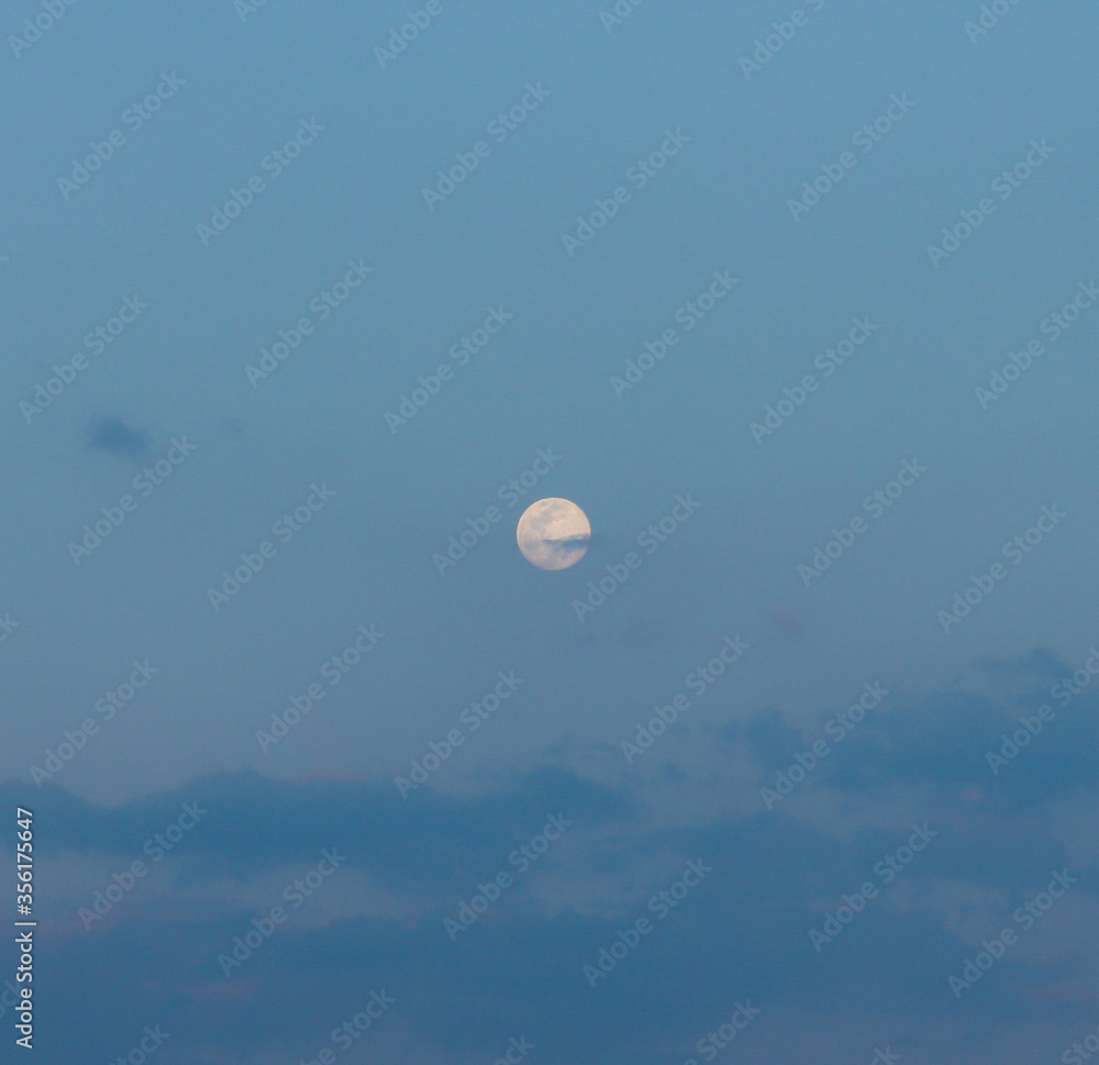 Big beautiful full moon in the blue cloudy evening sky with a cloud intersecting the supermoon in the middle. Natural satellite of Earth. Selective focus. Big beautiful full moon in the blue cloudy evening sky with a cloud intersecting the supermoon in the middle. Natural satellite of Earth. Selective focus.