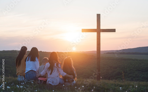 Christian family. Happy family on the nature. Wooden cross against the sky. Cross. Crucifixion on the background of the sky and sunset. Easter. Calvary.