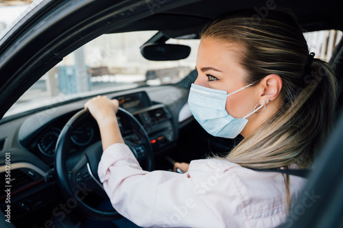  Woman with face mask driving her car during coronavirus pandemic